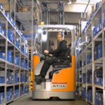 Operator driving Still electric forklift in narrow warehouse aisle
