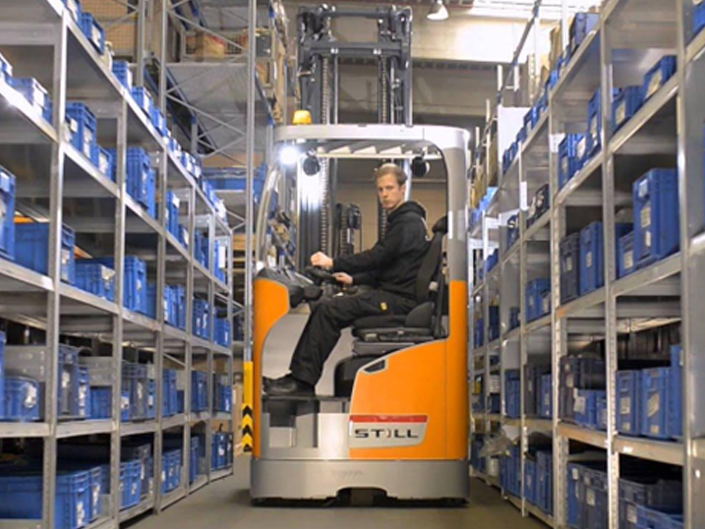 Operator driving Still electric forklift in narrow warehouse aisle